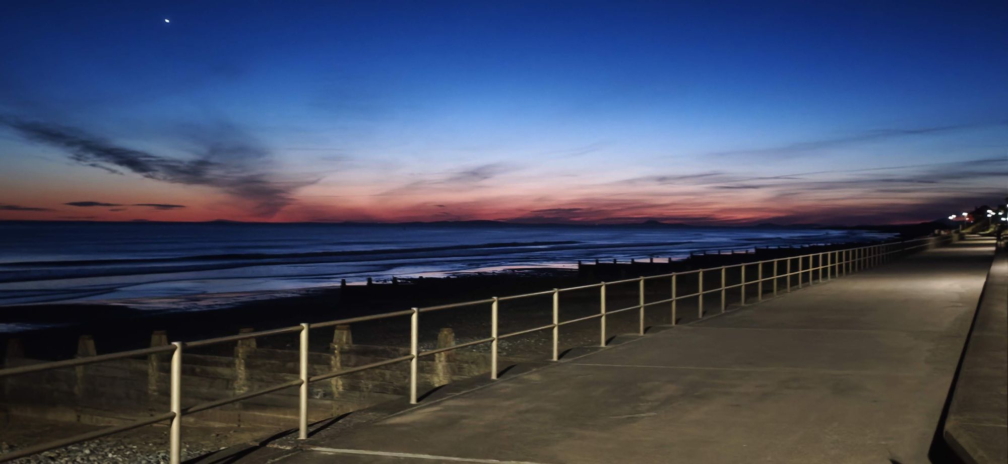 Tywyn promenade at dusk, with railings running along the beach and a pink and blue sky over Cardigan Bay