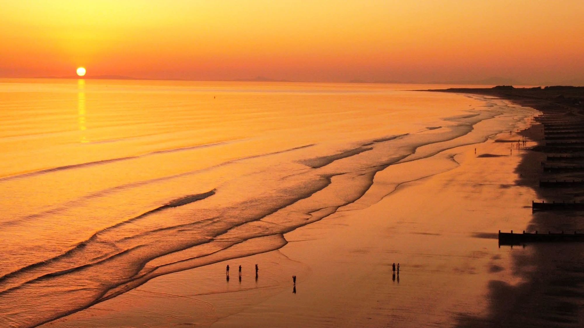The sun setting over Cardigan Bay, lighting the wet sand of Tywyn beach gold