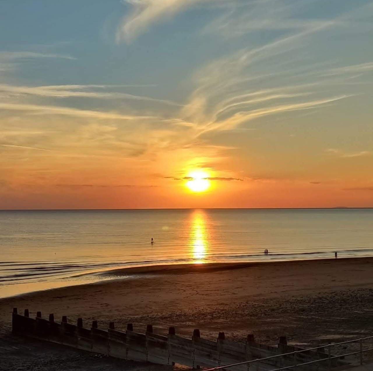 The sun setting over a calm sea, with wooden groynes on Tywyn beach in the foreground